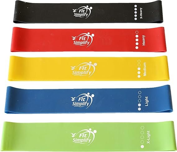 Set of 5 colorful Fit Simplify resistance bands placed on a yoga mat with a woman doing leg raises – great for belly fat workouts at home. belly fat